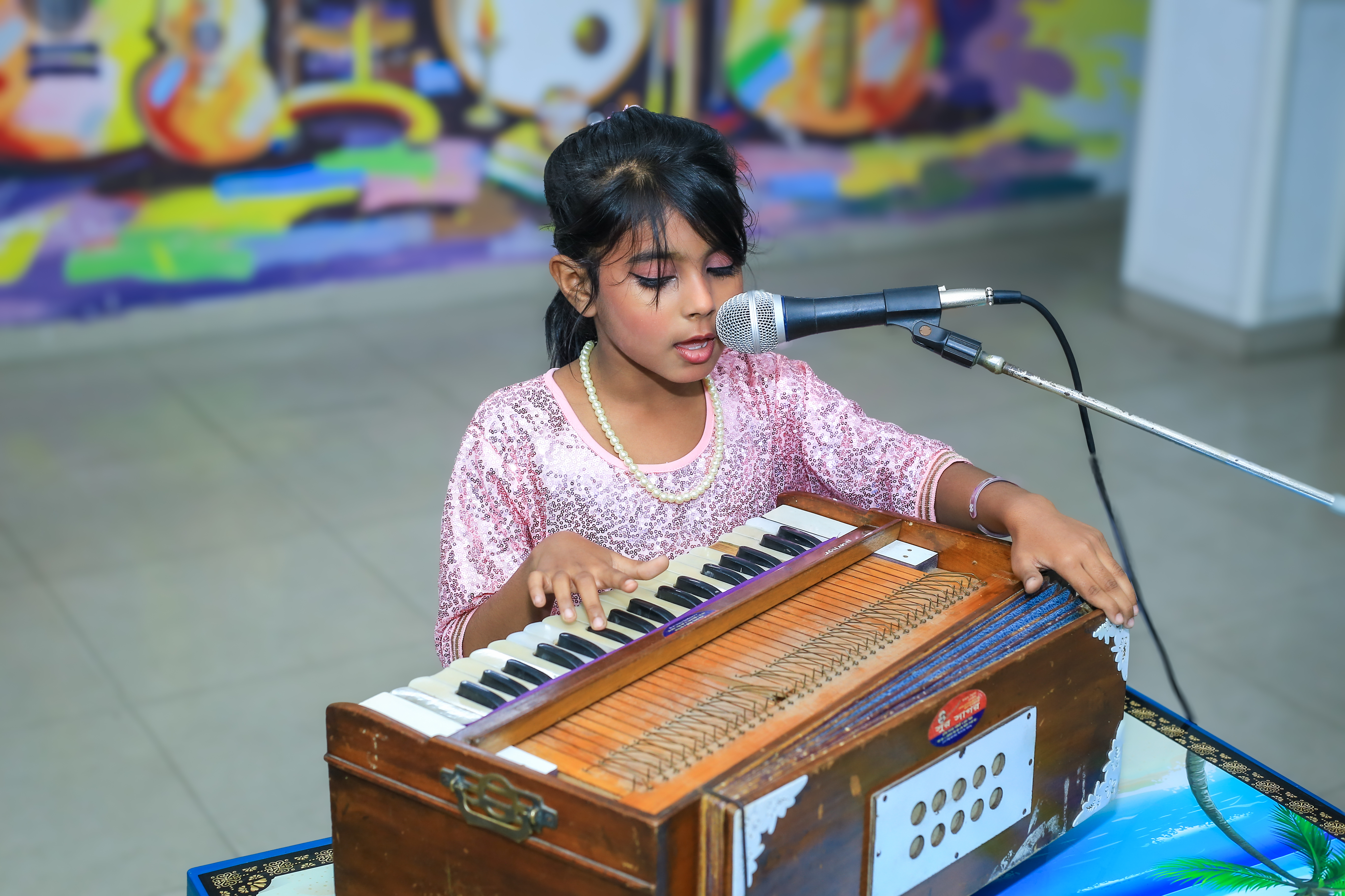 A young student playing harmonium and singing into a microphone